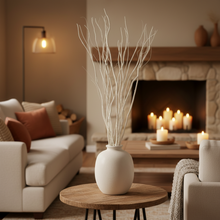 Load image into Gallery viewer, White vase with dried branches on a wooden table in a cozy living room with candles and a fireplace.