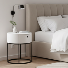 Load image into Gallery viewer, A modern bedside table with a white cylindrical top, black metal frame, and a single drawer, styled next to a bed in a minimalist bedroom.