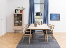 Load image into Gallery viewer, Dining room with wooden table and chairs, cabinet, and large window with blue curtains.