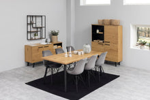 Load image into Gallery viewer, A modern dining room furniture set featuring a rectangular light oak wood table with six gray chairs, a matching sideboard, and a tall cabinet, arranged on a black rug in a bright room with gray walls.