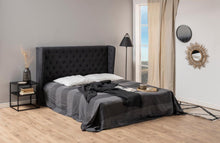 Load image into Gallery viewer, A modern bedroom scene featuring a bed with a tall, tufted dark gray headboard, dressed in a dark gray and black striped duvet cover with white pillows. The room has light wood floors, beige walls, a window with beige curtains, a black floor lamp, and a black metal side table.