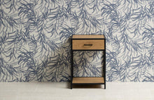 Load image into Gallery viewer, A small two-tier nightstand with a light oak wood drawer and shelves, supported by a black metal frame, set against a blue and white botanical patterned wallpaper.