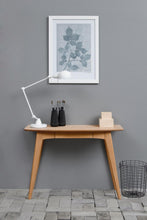 Load image into Gallery viewer, Wooden desk with lamp, plant artwork, and small items against a gray wall.