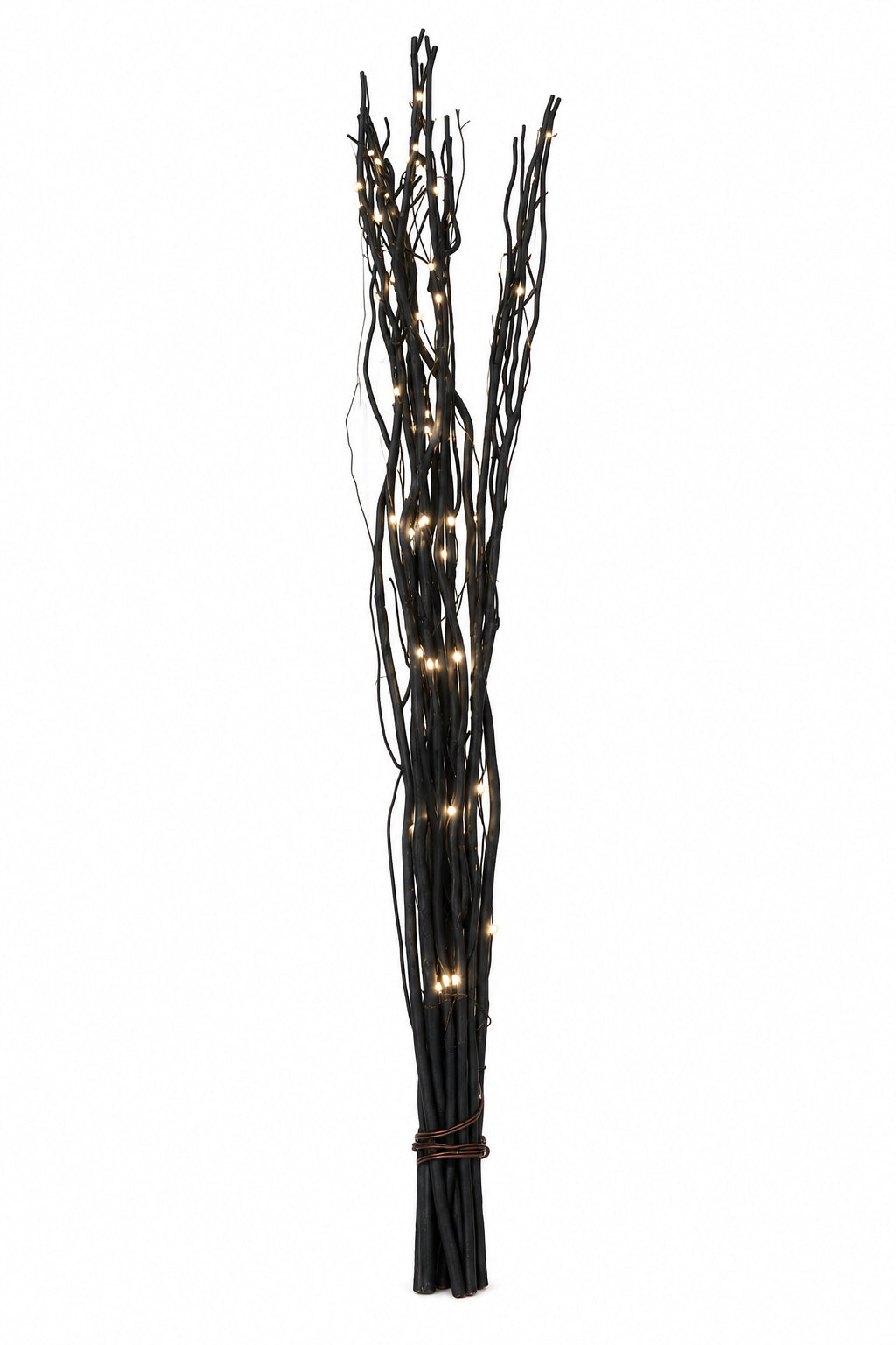 A bundle of black decorative branches or twigs with small warm white string lights woven through them, standing upright against a plain white wall.