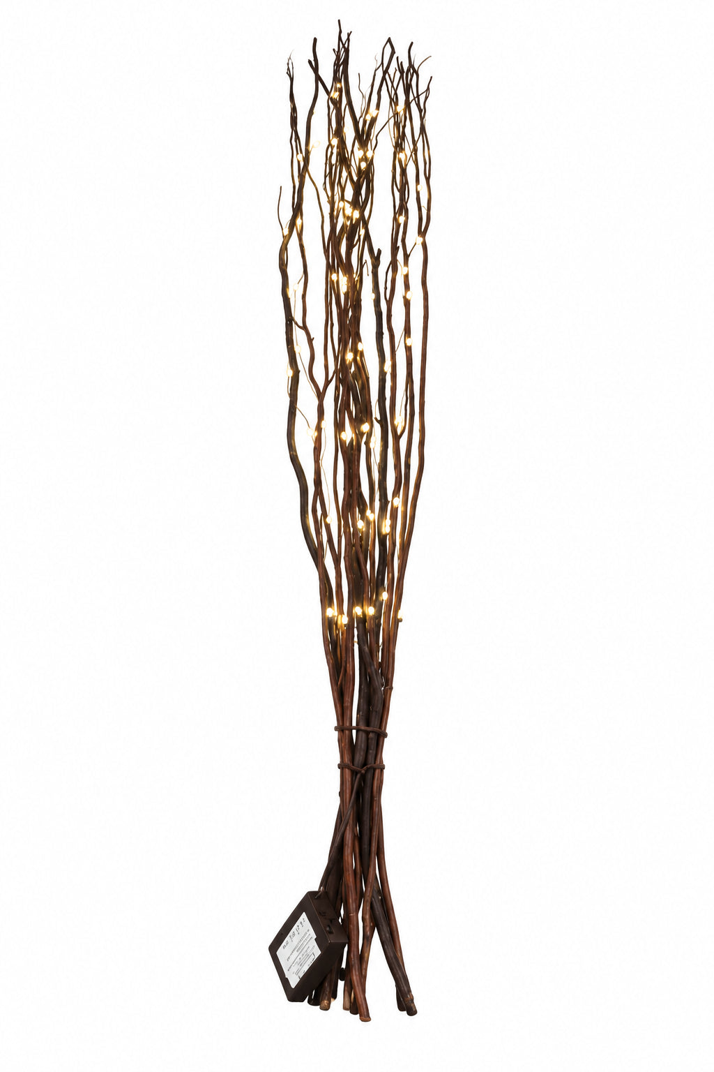 A decorative arrangement of tall, slender brown branches or twigs with warm white string lights woven through them, standing on a dark wooden surface against a plain off-white wall.