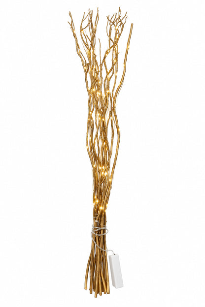 A decorative bundle of artificial gold branches with warm white string lights, tied at the base with a white tag, set against a plain white wall.