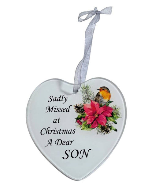 A heart-shaped glass hanging decoration with a white background, featuring a colorful poinsettia flower, a robin, and the text 'Sadly missed at Christmas a dear Son'.