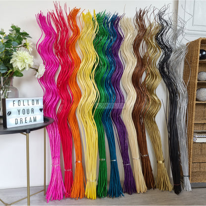 A selection of tall spiral willow twigs bunches dyed in various colors displayed vertically with a sign reading 'FOLLOW YOUR DREAMS' in the foreground.