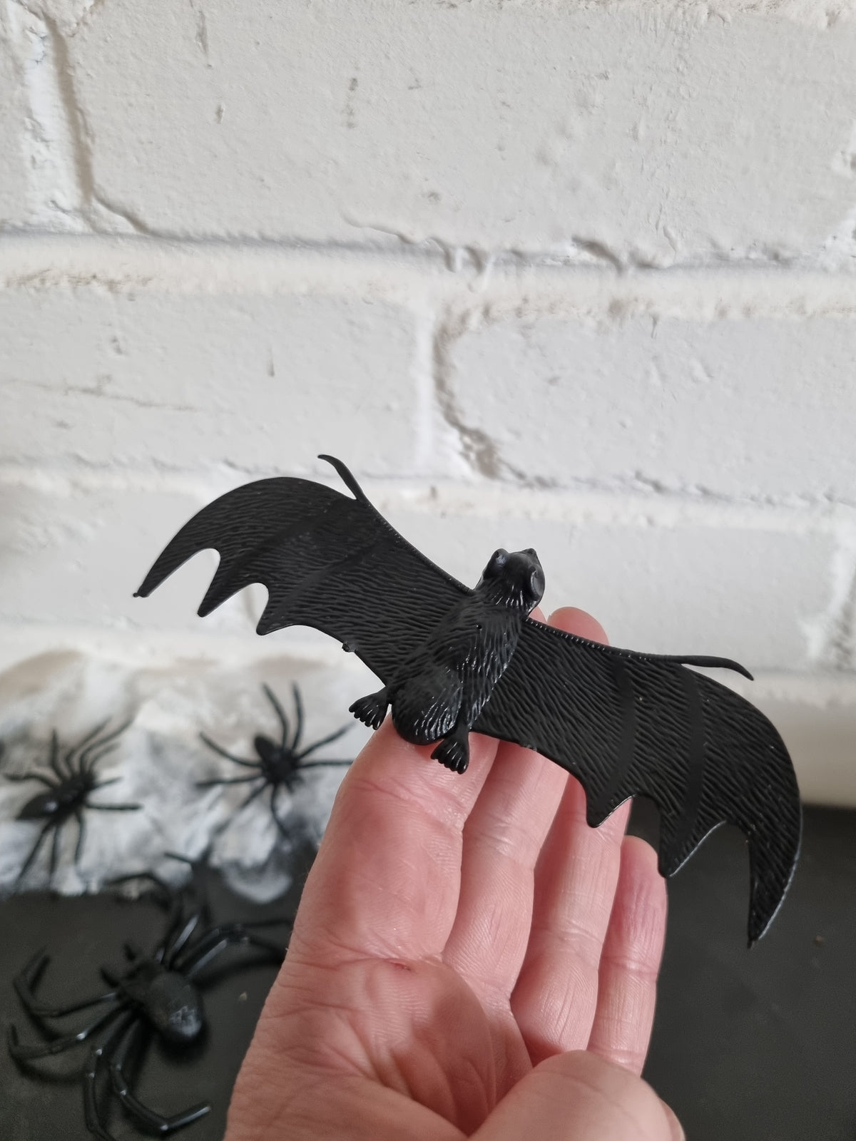A small black plastic raven figurine with wings spread, held in a person's hand against a white brick wall background.