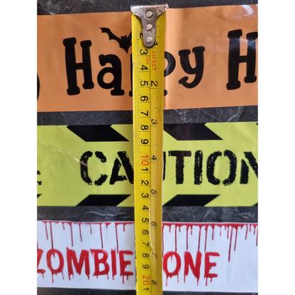 A yellow tape measure is shown vertically against Halloween warning signs that read 'Happy H' and 'CAUTION', with a white sign at the bottom reading 'ZOMBIE ONE'.