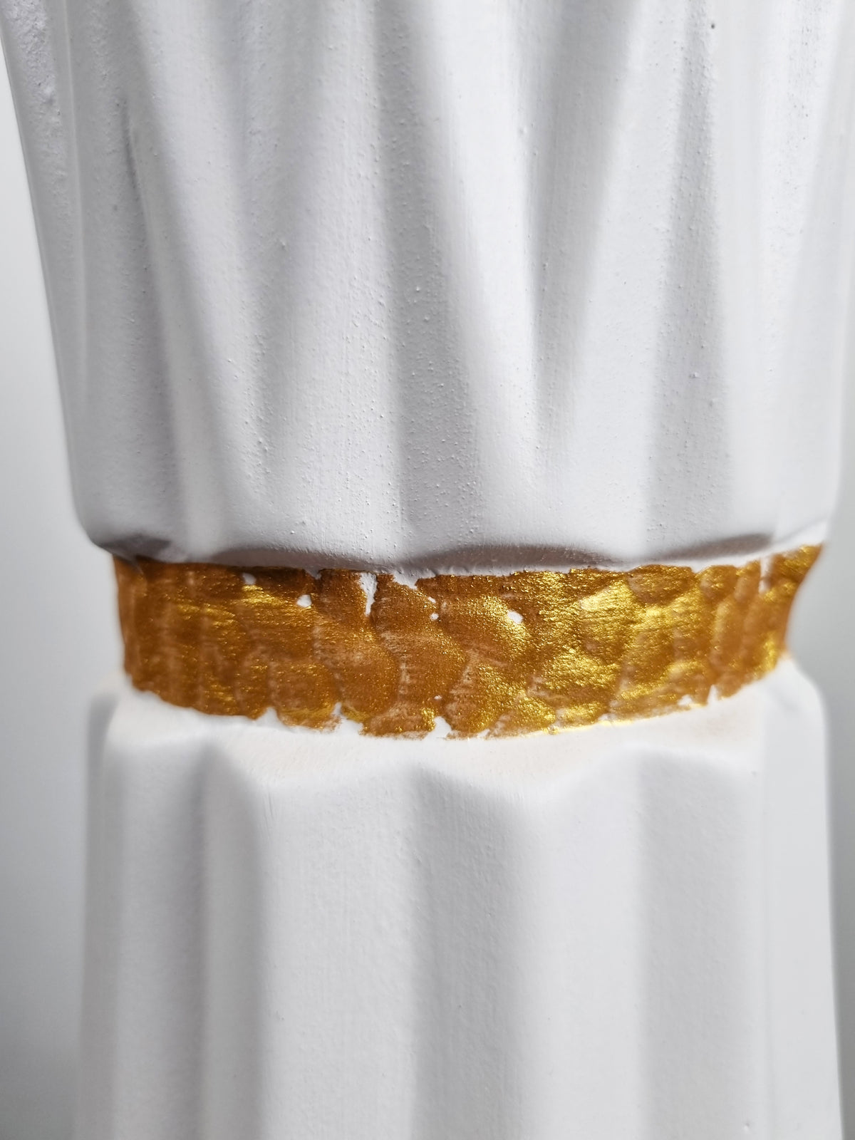 A close-up of a white fluted decorative vase featuring a textured metallic gold band around the middle.