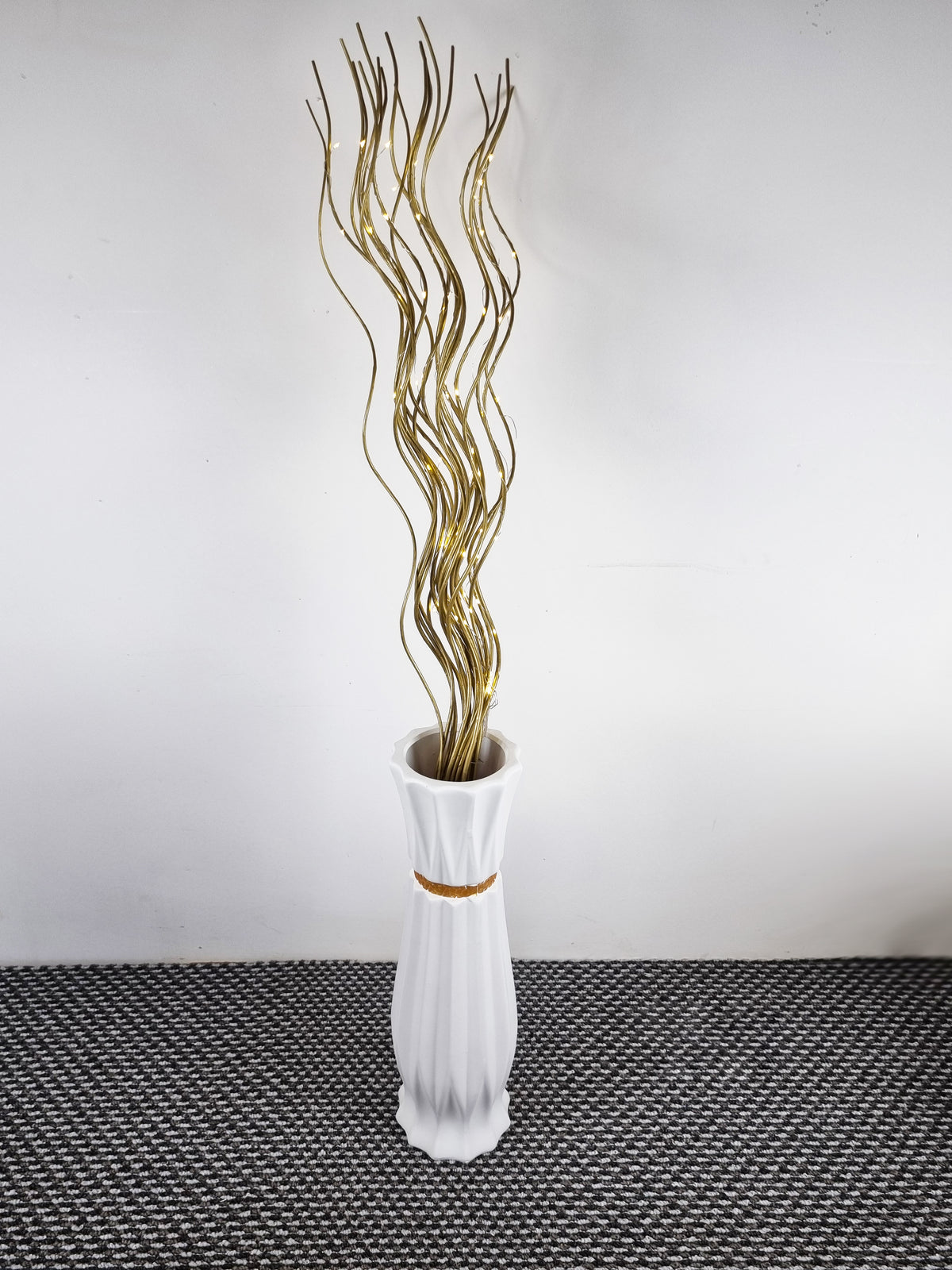 a white ceramic floor vase with spiral willow twigs inside
