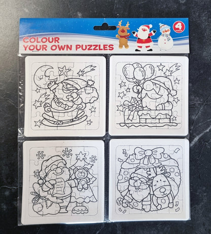 A package of four Christmas-themed colour your own puzzles on a dark marble surface. The packaging header is blue and red, and the four white puzzle cards feature black-and-white line drawings of Santa Claus, a reindeer, and a snowman.