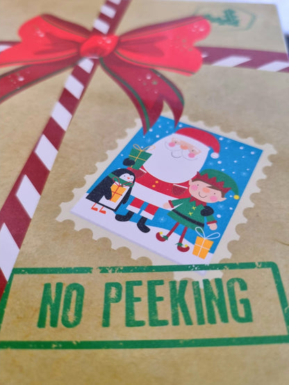 A close-up of a Christmas-themed gift box or card featuring a red bow, a postage stamp illustration with Santa Claus, a penguin, and an elf, and a green stamp-like border that reads “NO PEEKING.”.