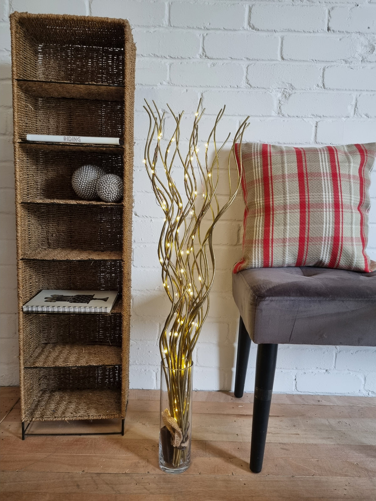 Decorative shelf with gold branch sculpture, plaid pillow, and suit jacket against a white brick wall.