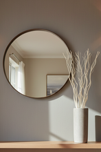 Load image into Gallery viewer, Round mirror on a wall with a vase of branches on a table below.
