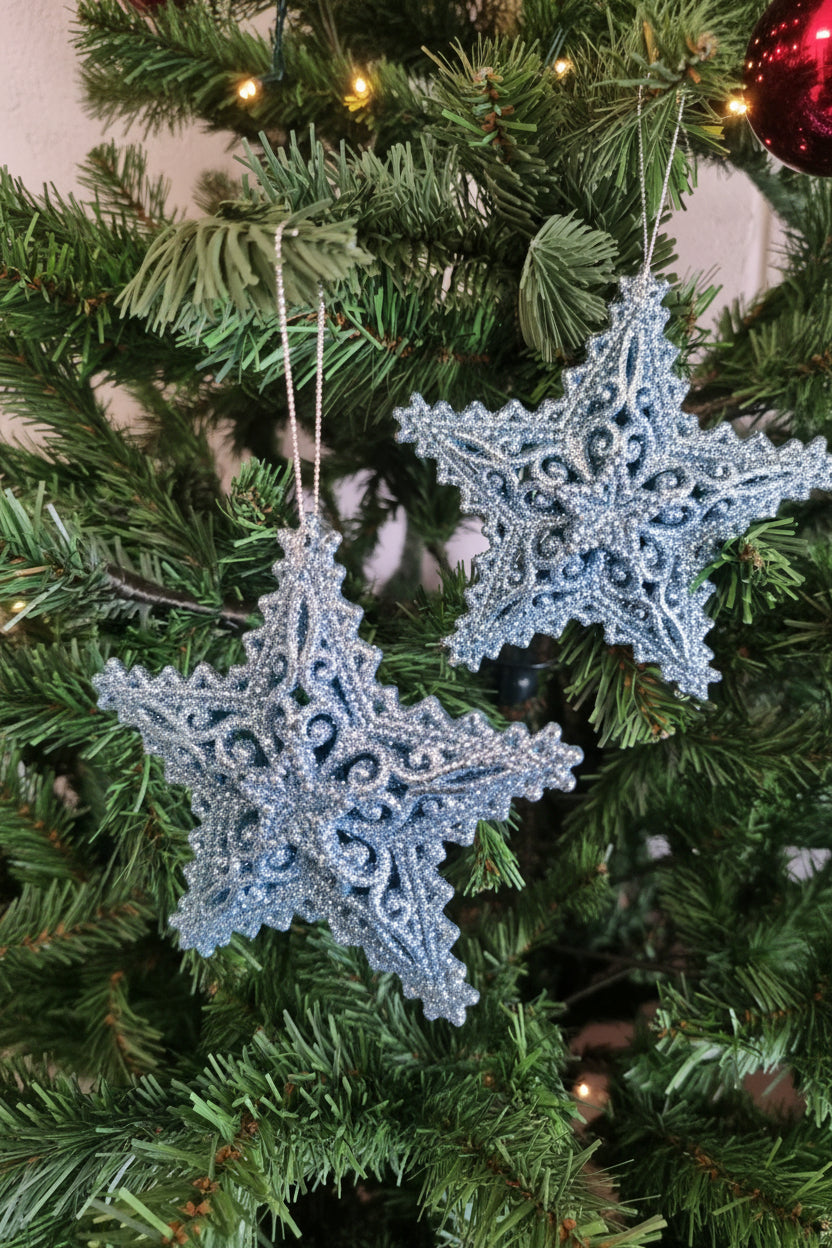 Two glittery light blue snowflake Christmas ornaments hanging on a green artificial Christmas tree.