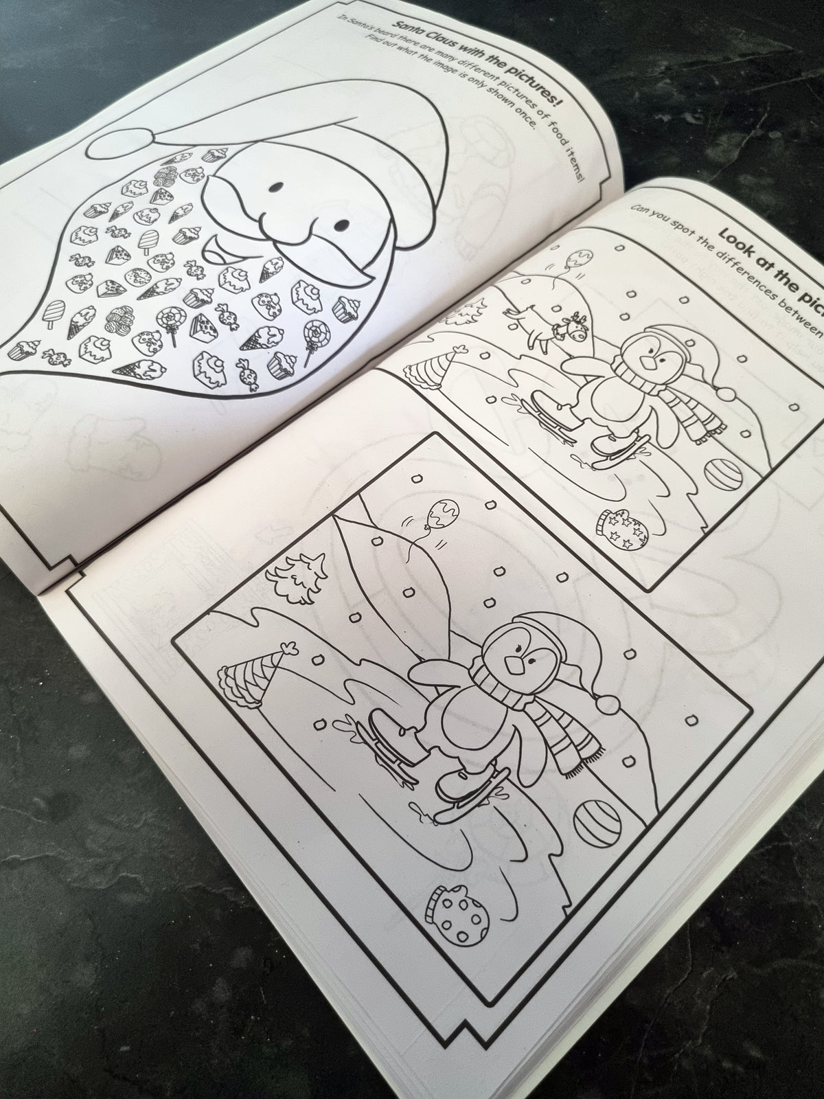 An open black-and-white coloring book or activity booklet showing holiday-themed illustrations, photographed on a dark textured surface.
