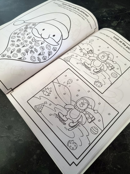 An open black-and-white coloring book or activity booklet showing holiday-themed illustrations, photographed on a dark textured surface.