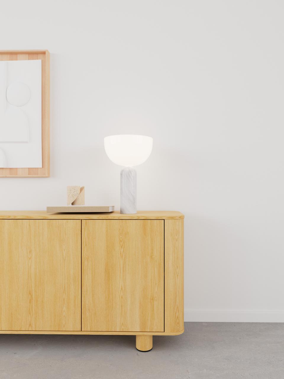 Wooden sideboard with a lamp and decorative items against a white wall.