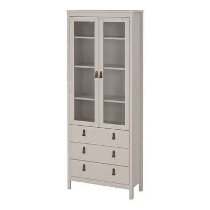 A tall, narrow storage cabinet in a light warm gray or greige finish, featuring two upper glass-front doors with shelves and three lower drawers with small dark metal handles, shown on a plain white background.