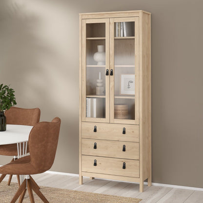 A tall light oak wood Barcelona display cabinet with two glass-front upper doors and three drawers below, styled in a dining room next to a table and chairs.