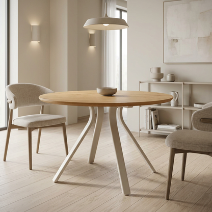 A round light oak Bristol dining table with sculptural grey splayed legs, surrounded by two upholstered dining chairs in a bright, modern minimalist dining room.