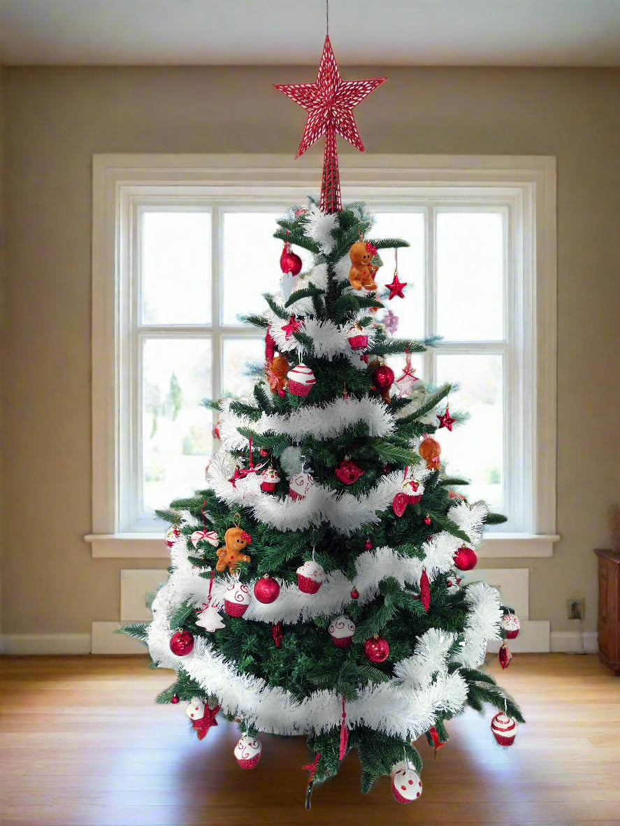 A decorated Christmas tree stands in a room with beige walls and a large window behind it. The tree is green with white fluffy garlands and red ornaments, topped with a red star.