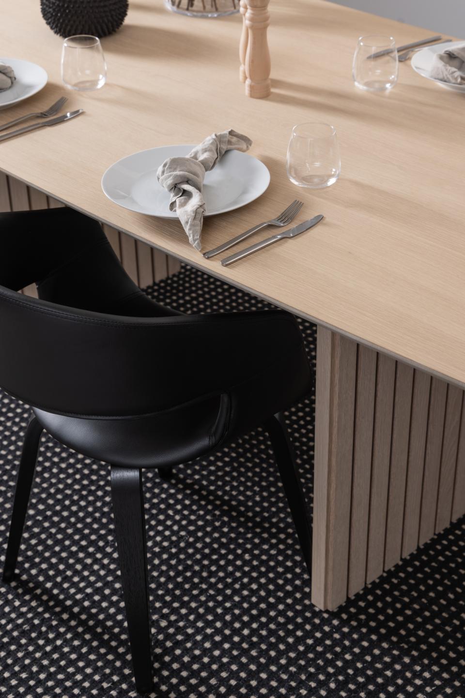 Dining table with plates, cutlery, and a black chair on a patterned floor.