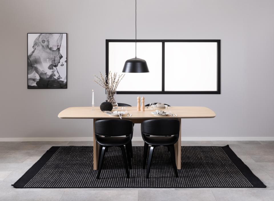 Dining area with a wooden table and black chairs against a gray wall with framed pictures.