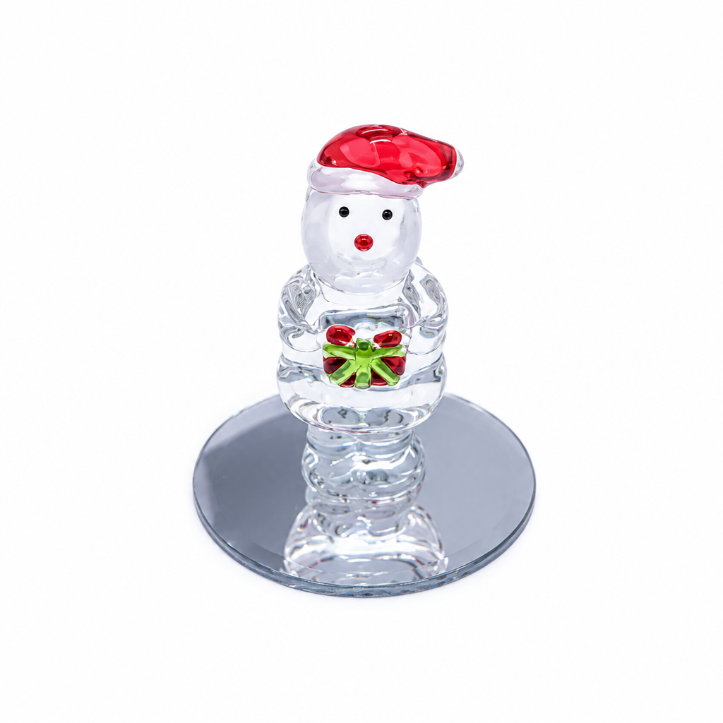 A clear glass Santa Claus figurine wearing a red Santa hat and holding a green gift box with red and white accents, standing on a round mirrored base against a white background.