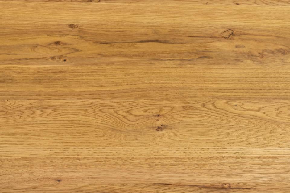A close-up view of a warm honey-toned wood surface with visible grain, knots, and natural texture.