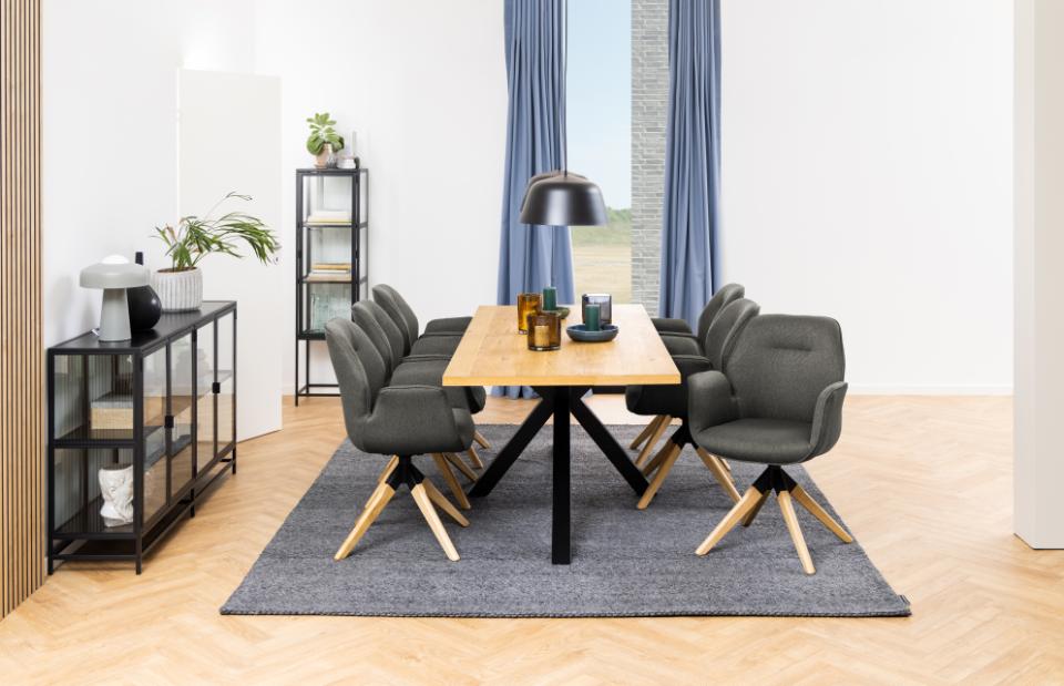 Dining room with a wooden table and gray chairs on a rug, large windows with blue curtains.