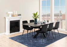Load image into Gallery viewer, Dining room with a black table and chairs on a blue rug, large windows, and a fireplace.
