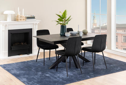 A modern dining set featuring a rectangular black ceramic table and four black chairs, styled on a blue rug in a bright room with a fireplace and large windows.
