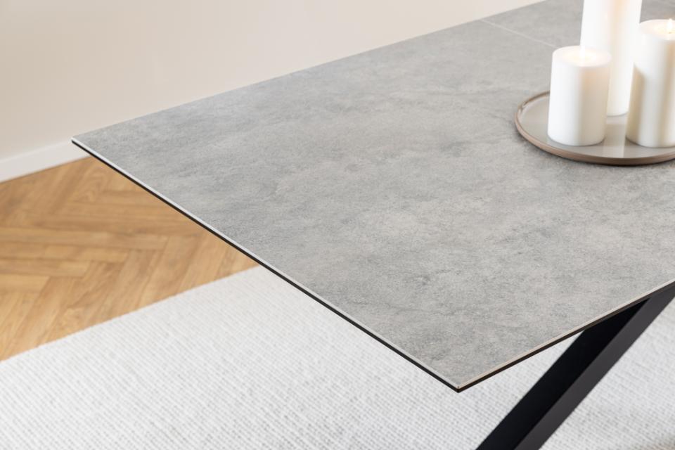 A grey ceramic table top in a modern room setting with a light wood herringbone floor, white rug, and white pillar candles on a tray.
