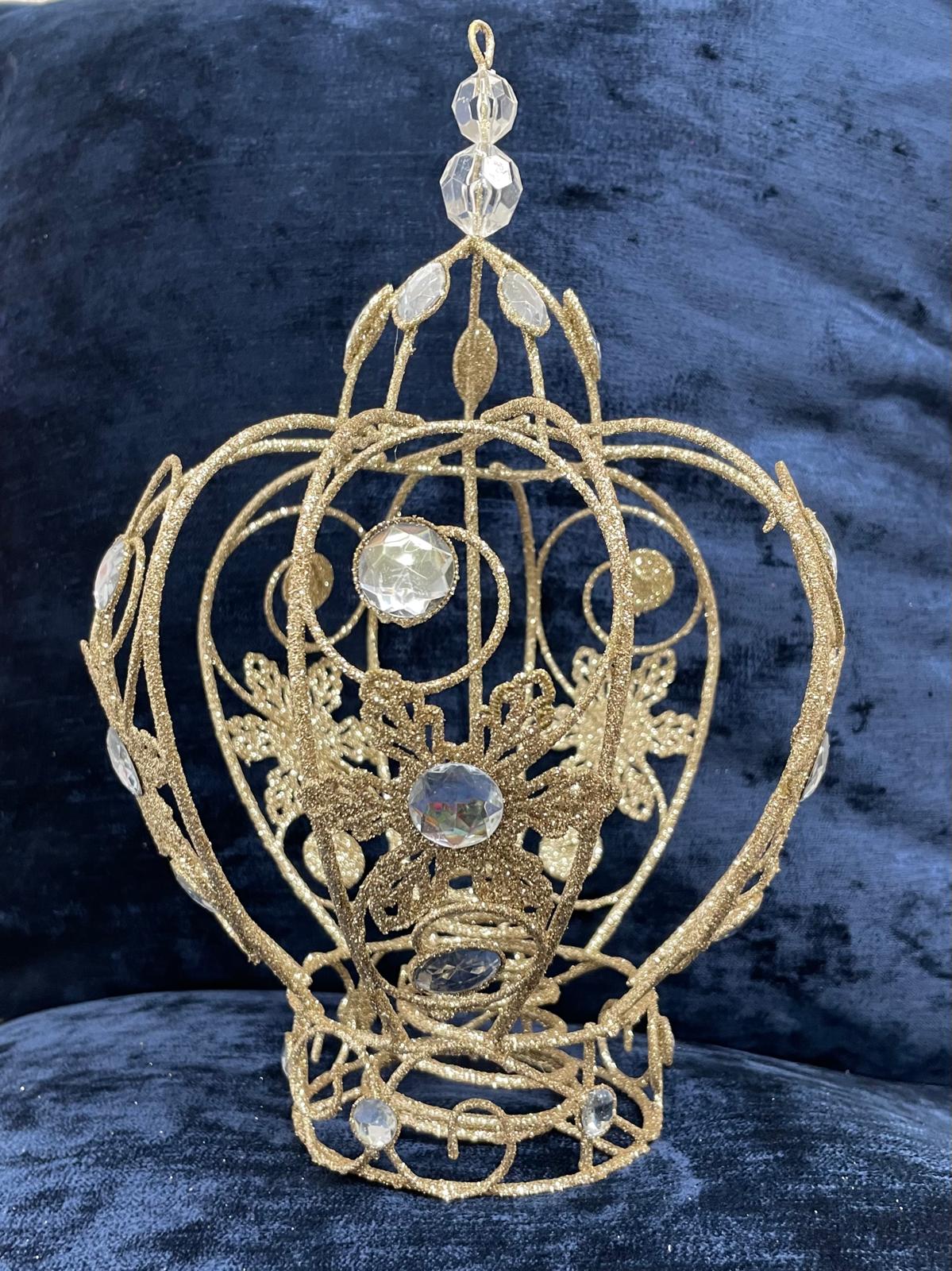 A gold filigree crown ornament with clear faceted crystal-like accents, displayed against a dark blue velvet background.