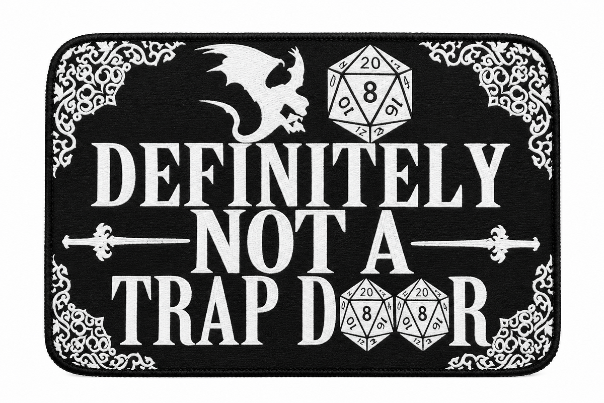 A rectangular black mat or sign with rounded corners, featuring white fantasy-style text reading “DEFINITELY NOT A TRAP DOOR,” a white dragon illustration, a white d20 die, a white d8 die, and ornate corner flourishes.