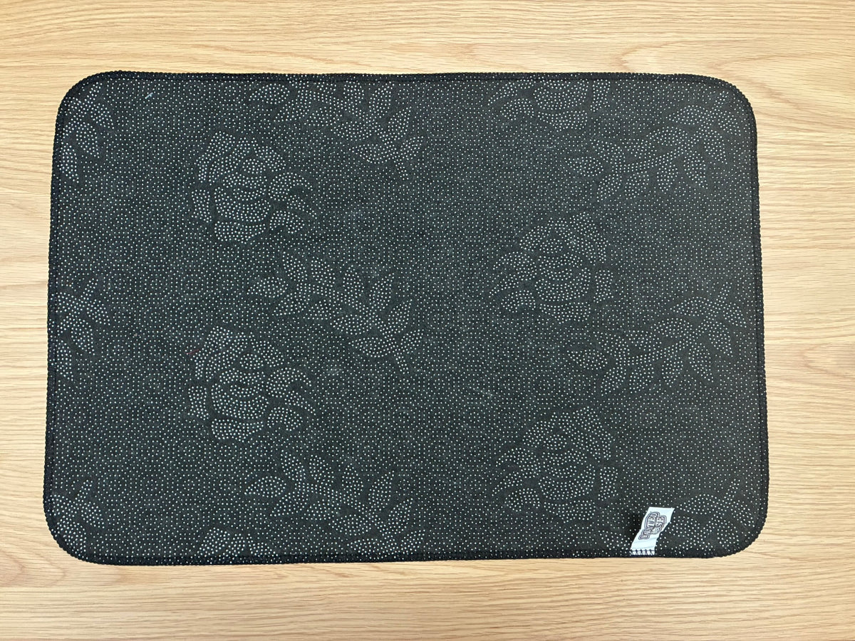 A rectangular black mouse pad with a subtle circular floral pattern, laid flat on a light wood surface.