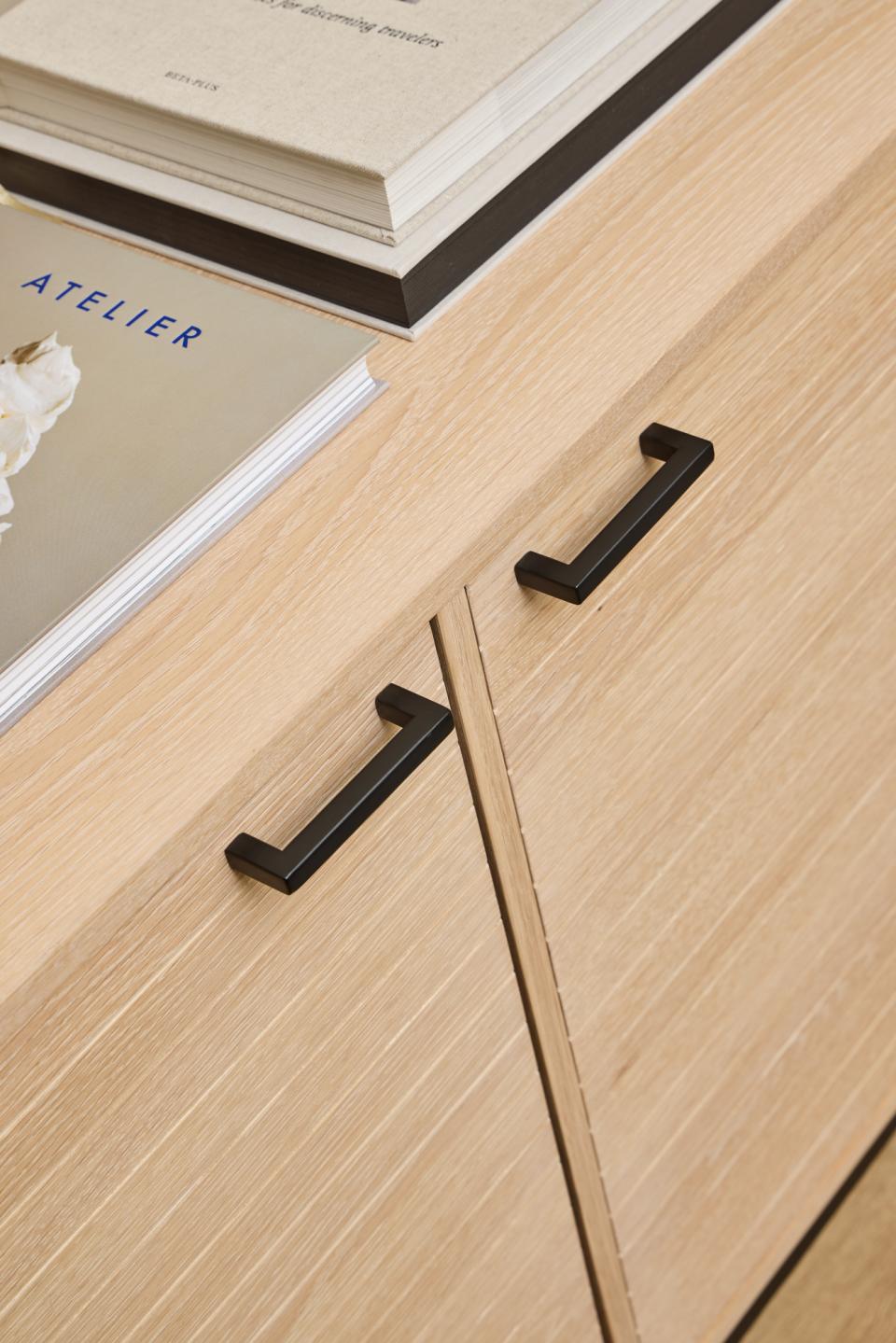 Close-up of wooden doors of a sideboard with black handles and a book on top.