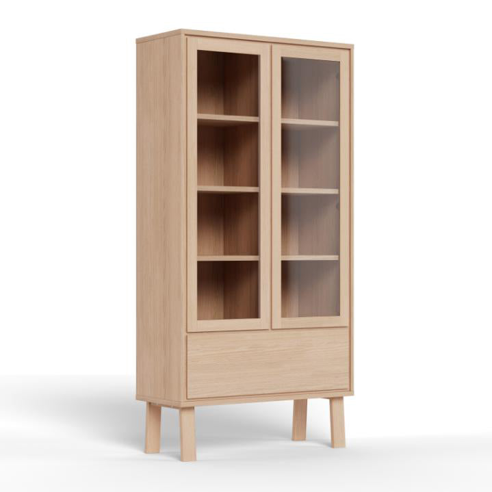 A tall light oak wood display cabinet with two glass-front doors, four interior shelves, and a lower drawer, shown on a white background.