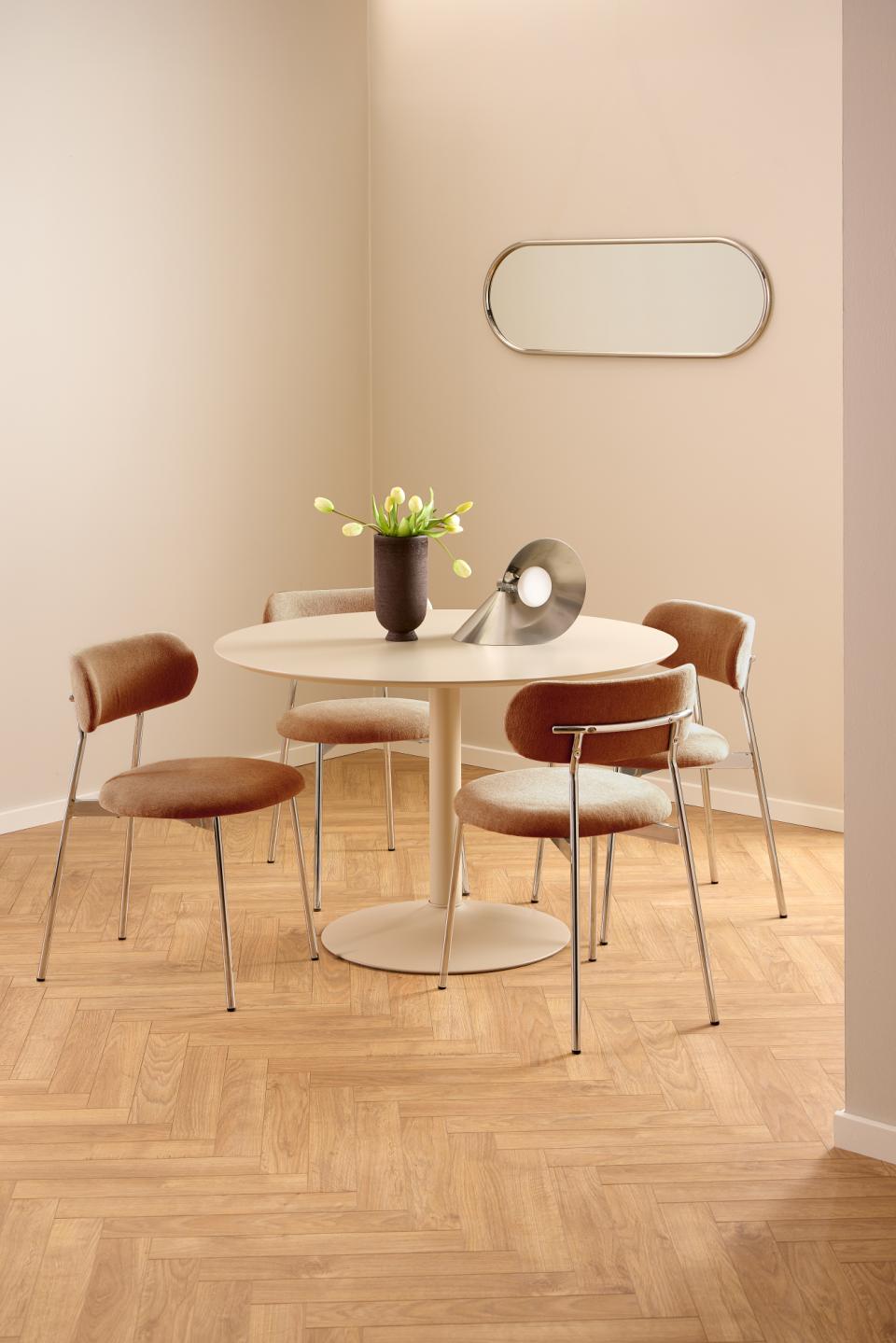 Dining area with a round table and four chairs in a room with beige walls and wooden flooring.