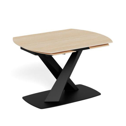A modern oval rectangle extending dining table with a light natural wood top and a black metal X-shaped pedestal base, shown on a plain white background.