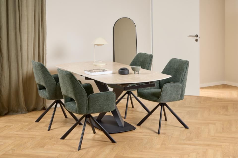 A modern dining set featuring a rectangular extending ceramic table with a black metal base and four dark green velvet swivel chairs with black metal legs, shown in a styled dining room with wood floors and neutral walls.