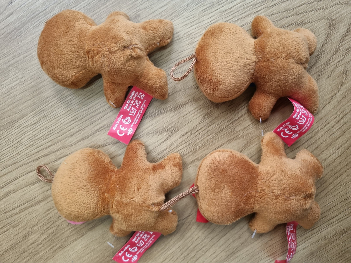 Four small plush animal toys in a light brown/tan color, arranged on a light wood surface. Each toy has a pink tag attached.