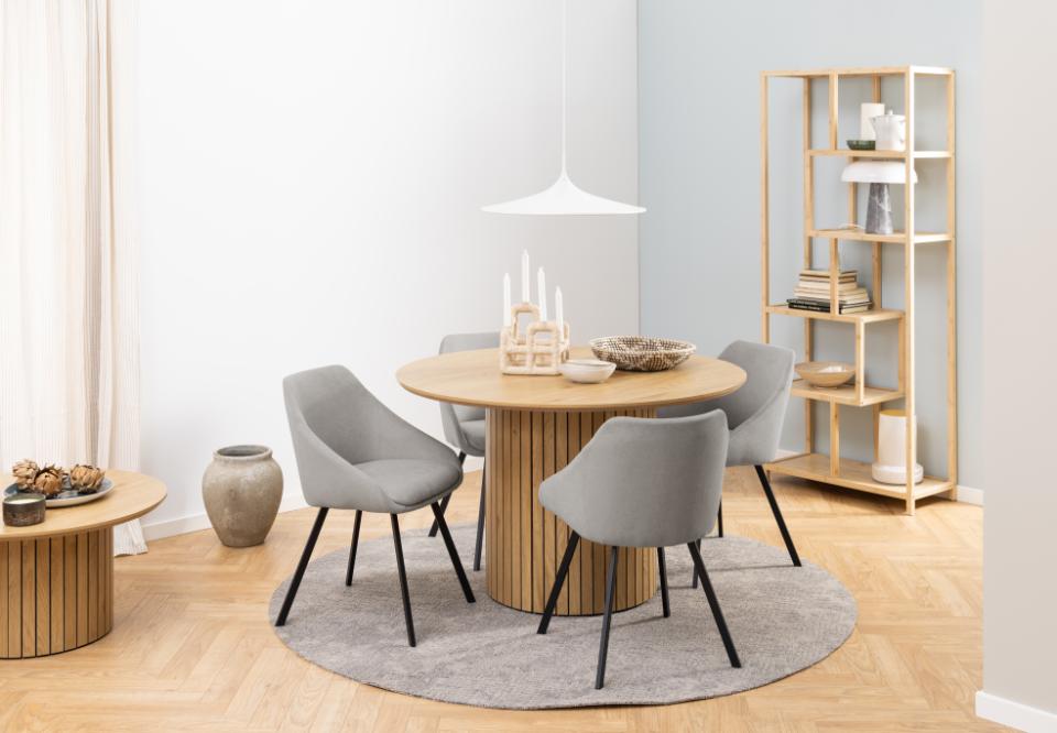 Dining room with round wooden table and gray chairs, wooden shelf, and light decor.