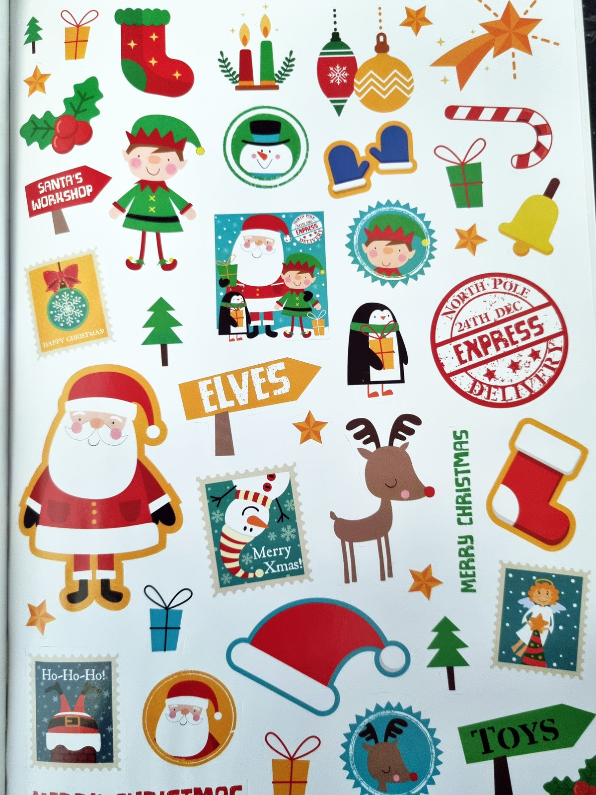 A sheet of Christmas-themed stickers featuring Santa Claus, elves, reindeer, stockings, candy canes, snowman, penguin, stars, trees, and holiday text on a white background.