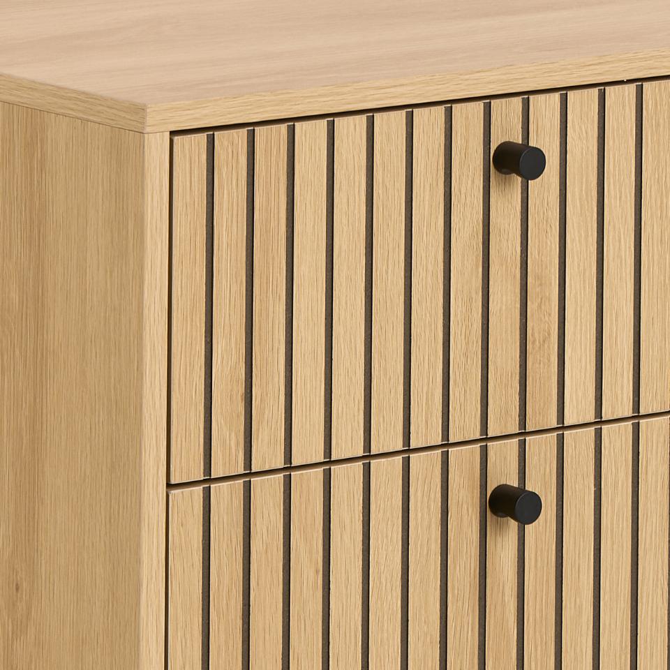 Close-up of a light oak wood cabinet with vertical slat panel doors and round black knobs.