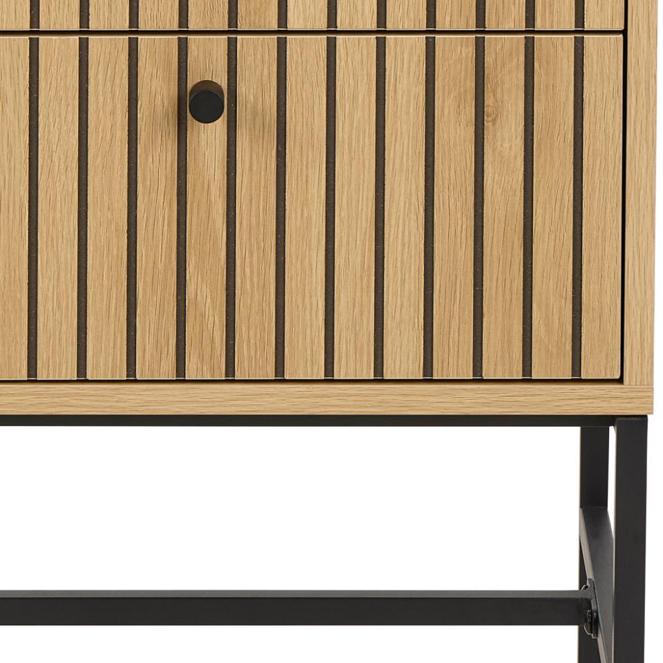 Close-up of a wooden cabinet with vertical slat detailing, a round black knob, and a black metal frame leg against a white background.