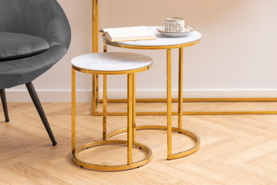 Gold side table with marble top next to a gray chair on a wooden floor.